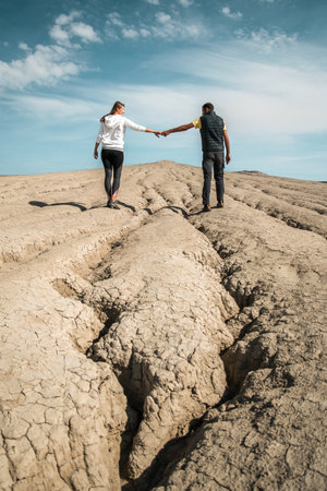Young couple walking together on cracked dry soil, picture taken in the mud volcanoes park in Romaniaの写真素材