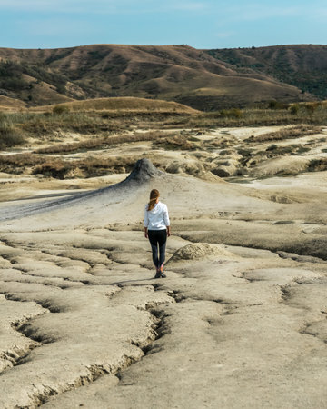 Young girl facing a mud volcano standing on cracked dry soil, Romaniaの写真素材