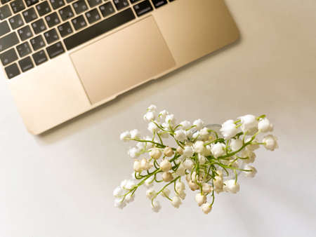 Background with laptop and lily of the valley. Work from home. Fresh spring flowers in the glass