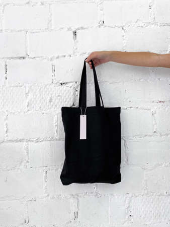 Womans hand holding a new black tote bag or shopper with blank labelの写真素材