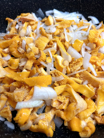 Chanterelle mushrooms. Cooking. Chopped mushrooms with onions in black cast-iron frying pan. Process of roasting mushrooms. Food background with yellow mushrooms. Top view.の写真素材