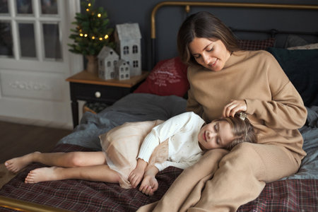 Mother relaxing with daughter on cozy bed during winter evening