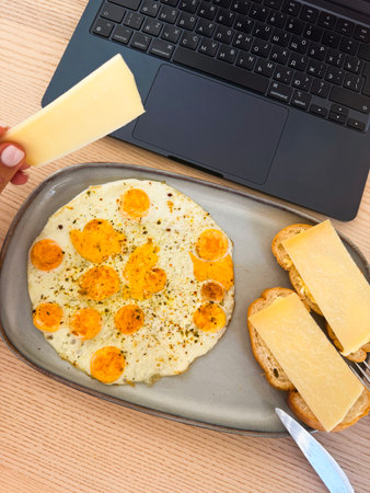 Delicious homemade breakfast with eggs and cheese in a cozy workspace settingの写真素材