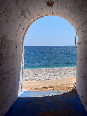 View of the serene beach through an archway leading to the ocean on a sunny dayの写真素材