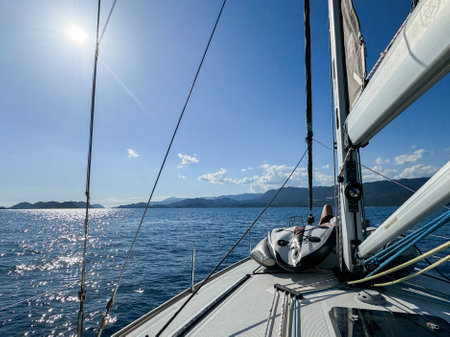 Sailing across calm waters under a bright sun in a picturesque coastal landscapeの写真素材
