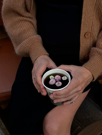 Woman holds cup of tea with flowers in outdoor setting on a cool afternoonの写真素材
