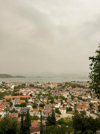 Scenic view of a coastal town under cloudy skies with hills in the background