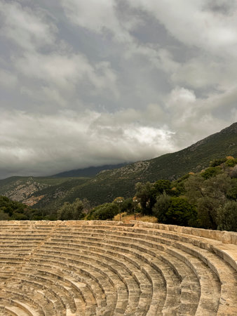 Ancient theater ruins surrounded by mountains under an overcast sky