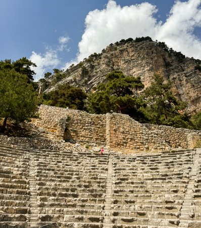 Visitors wander the steps of an ancient stone theater, surrounded by lush trees and towering...