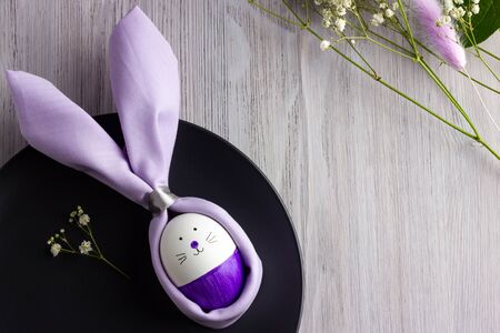 Easter table set with napkin Easter Bunny on a dark plate, white wooden background