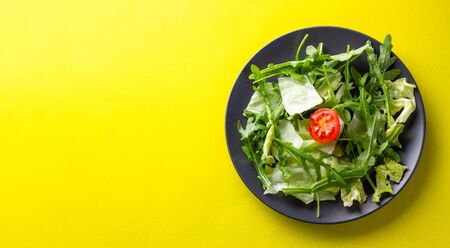 Fresh green salad with cherry tomato on yellow backdrop.の写真素材