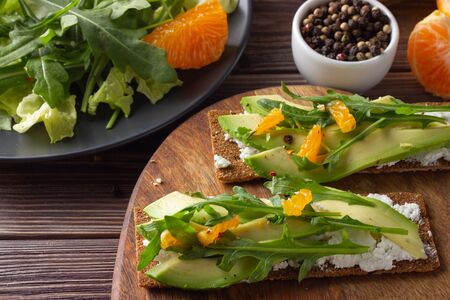 Wholegrain crisp bread with cheese, fresh rocket leaves, avocado and tangerine with green salad on...