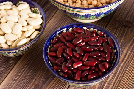 Red beans in a bowl among bowls of different legume on wooden background. Close up.