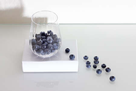 Blueberries in a glass on a white glass table.の写真素材