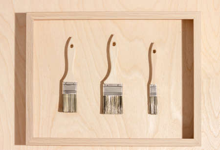 New paint brushes in a wooden frame, wooden background. Home renovation or DIY concept, flat lay.