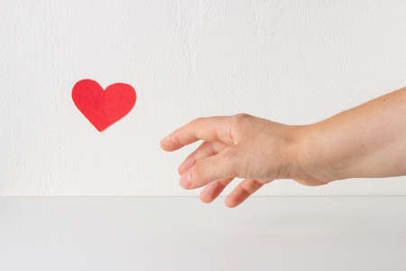 Womans hand with little red heart symbol. Womans hand reaches for heart symbol. Charity, life saving...