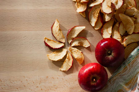 Dried slices of apple, laid out in the form of a flower and red apples on the table. Top view, copy...