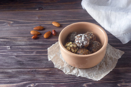 Healthy energy candies with oatmeal, cereals, chia seed, coconut flakes, cocoa and dried fruits in bowl with almond on wooden table. Copy space.の写真素材