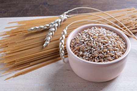 Spelt spaghetti and bowl with uncooked spelta grain and ears on wooden table.の写真素材