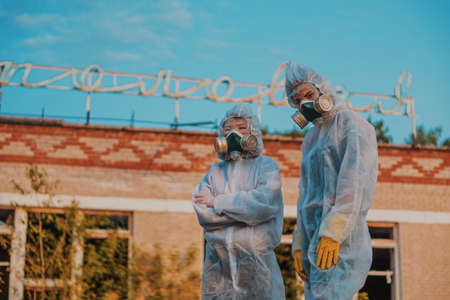 Two scientists put on a respirator and a radiation protective suit. Stern look into the camera from the abandoned territory. Care about ecology in bright saturated photos.の写真素材