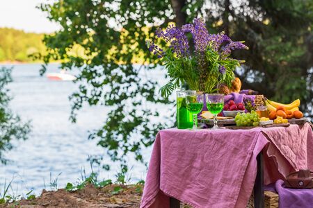picnic near water at table with flowers in forest fruits and vegetablesの写真素材