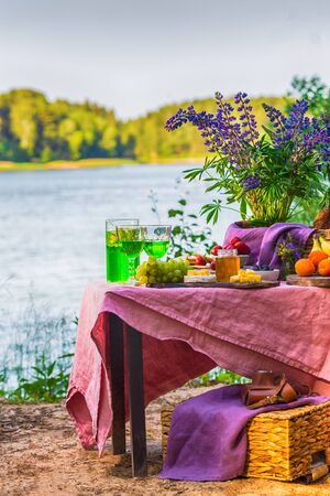 picnic near water at table with flowers in forest fruits and vegetablesの写真素材
