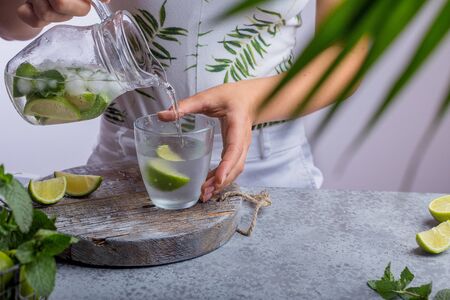 Young woman pouring fresh lemonade from jug into glassの写真素材