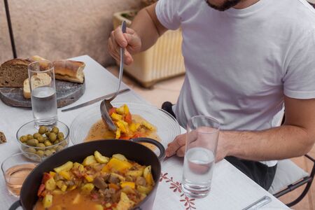 Man with barber in white t-shirt is in process of eating cooked vegetables family dinnerの写真素材