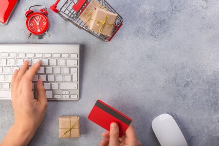 Woman hands ordering gifts online, paying by credit card. Concept online shopping buying presents. Red credit card, keyborad and christmas presents on grey table flat lay, copy space. Business christmas holidays concept, holiday gift online shopping concept. Save time.の写真素材