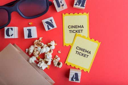 craft bag with popcorn 3d cinema glasses tickets wooden cubes with text on red background creative flatlayの写真素材