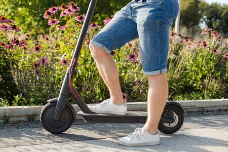 Man riding an eco-friendly electric kick scooter in a park in sunny weather on sidewalks