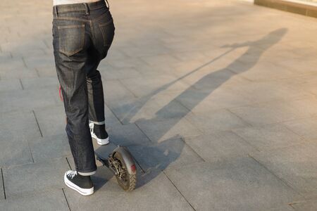 Girl riding an eco-friendly electric kick scooter in a park in sunny weather on sidewalks