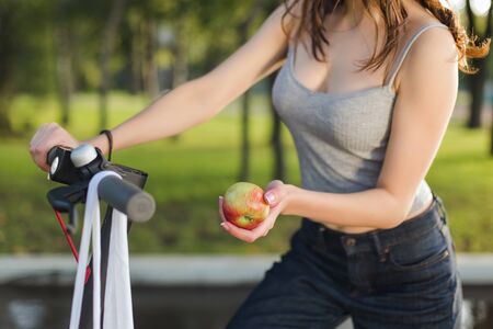 Close-up brunette girl with her electric scooter in a park holding an apple in her handの写真素材