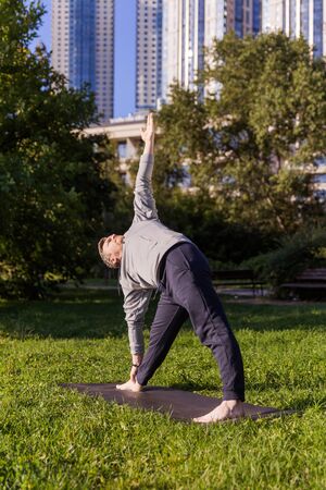 Inspired man doing yoga asanas in city park. Fitness outdoors and life balance concept. Stretching. Triangle Pose or Trikonasanaの写真素材