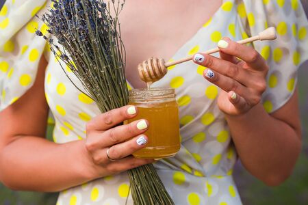 A girl in dress stands in the middle of a lavender field. In her hands is a bouquet of lavender and...