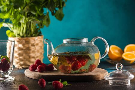 teapot with raspberry tea mint leaves and lemon on blueの写真素材