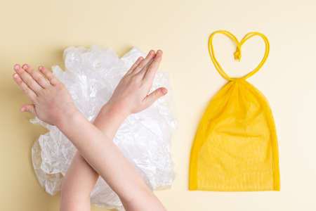 Yellow mesh reusable bag vs a lot of plastic bags little girl hands make sign to stop pollution