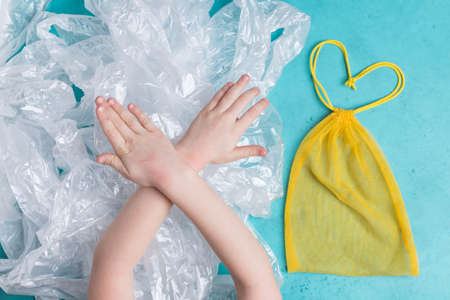 Yellow mesh reusable bag vs a lot of plastic bags little girl hands make sign to stop pollutionの写真素材