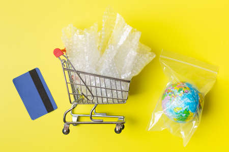 Metal shopping trolley with plastic waste and earth packaged in plastic bag credit cards, environmental concernの写真素材