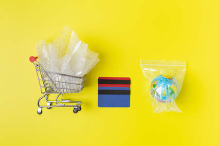 Metal shopping trolley with plastic waste and earth packaged in plastic bag credit cards,...