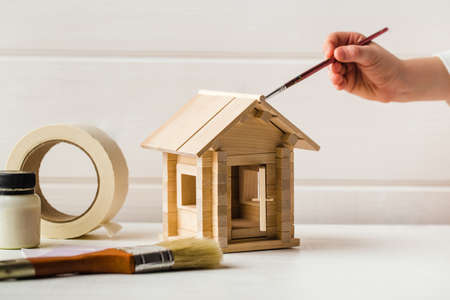 Child hands with toy wooden house and paint brush, home services conceptの写真素材