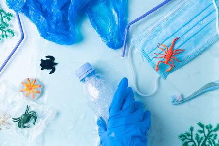 Pollution concept. Hand in blue glove takes plastic bottle from the ocean small marine fishesの写真素材
