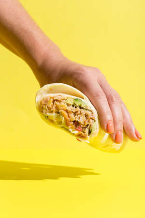 Hand takes doner roll shawarma with chicken and vegetables on yellow. High quality photoの写真素材