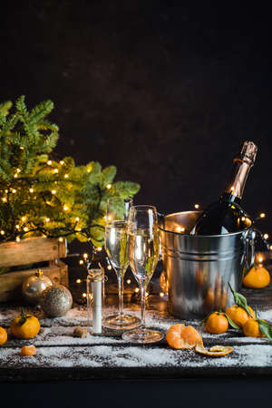 Still life with champagne bottle standing in a bucket with ice, two full flutes, LED lights and Christmas ornaments.の写真素材
