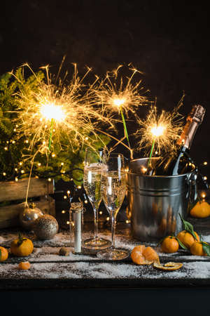 Still life with champagne bottle standing in a bucket with ice, two full flutes, sparklers and Christmas ornaments.の写真素材
