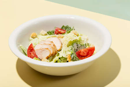 Caesar salad in white plate on yellow hard shadow modernの写真素材