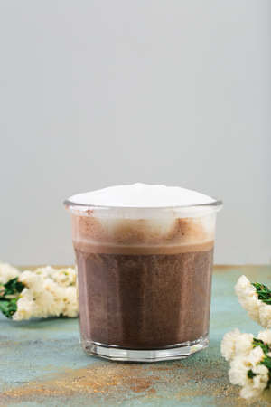 Cafe latte macchiato in a see through glass coffee cup. With flowers on the table next to the cup.の写真素材