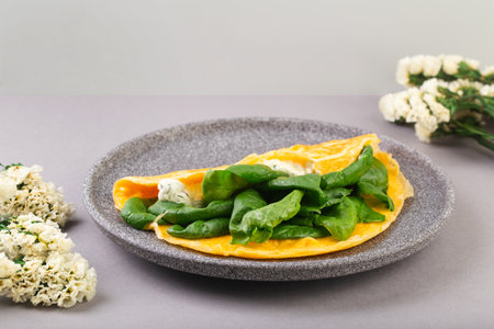 Omelette stuffed with spinach and cheese for a breakfast, with flowers on tableの写真素材