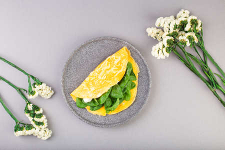 Omelette stuffed with spinach and cheese for a breakfast, with flowers on tableの写真素材
