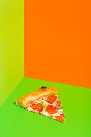 Piece of fresh tasty pepperoni pizza on green and orange background with copy space.の写真素材